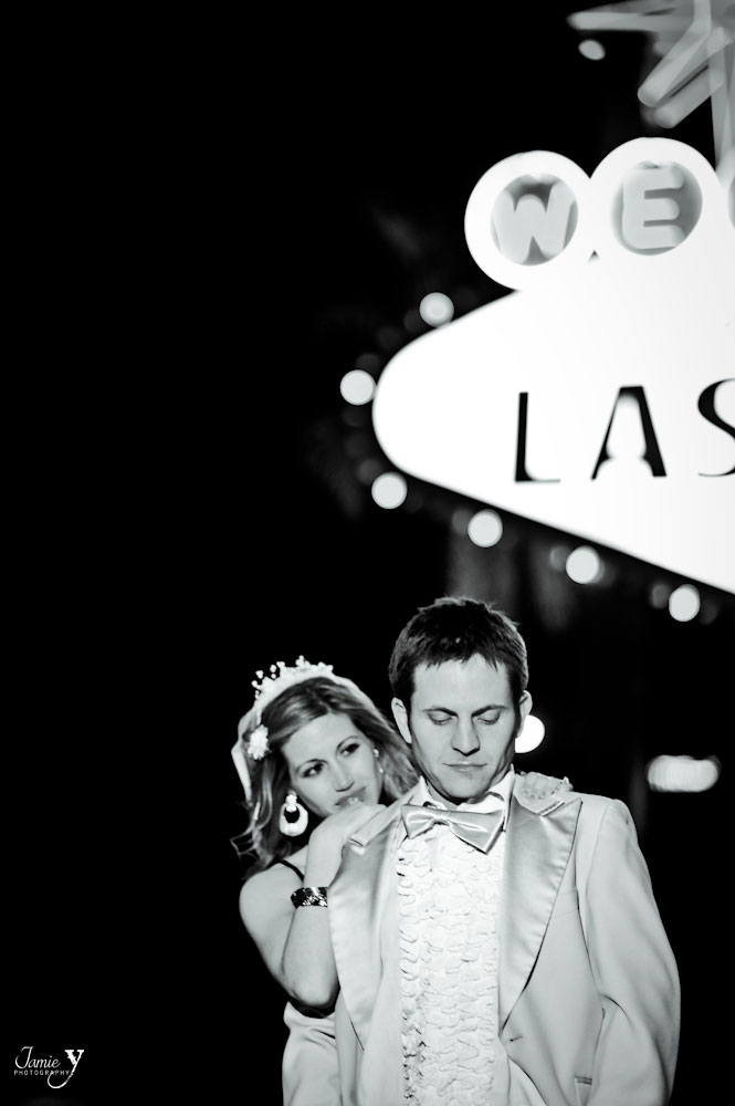 Las Vegas wedding photographer took picture of bride and groom at welcome to las vegas sign in black and white with bride standing behind groom and smiling