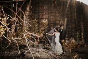 boho bride standing with groom on her wedding day holding veil in front of mining town