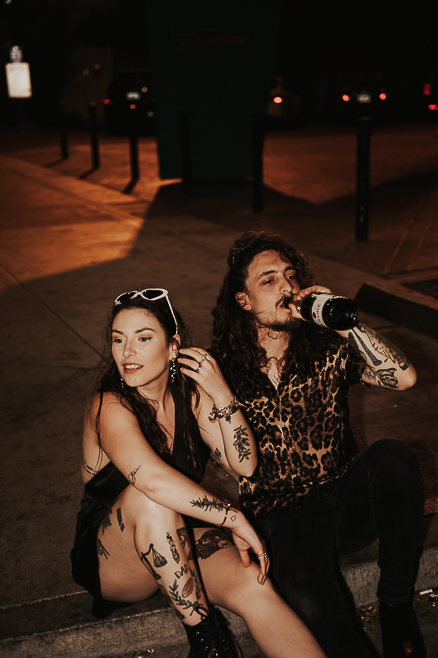 bride and groom in black sitting on curb in downtown las vegas drinking a beer