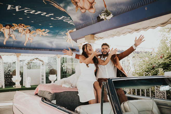 bride and groom sitting on back of pink cadillac at little white chapel in vegas