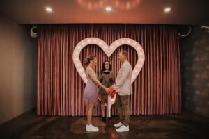 bride and groom in colorful clothes at sure thing chapel in front of heart